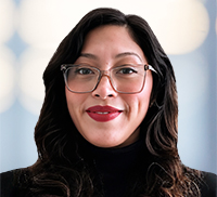 Portrait of a woman with dark wavy hair and glasses wearing a black top.