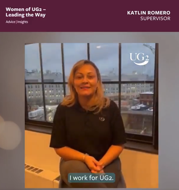 A woman sits in front of a window wearing a black UG2 shirt. Text reads "Women of UG2 – Leading the Way" and "KATLIN ROMERO SUPERVISOR." Subtitles: "I work for UG2, where women are truly leading the way.