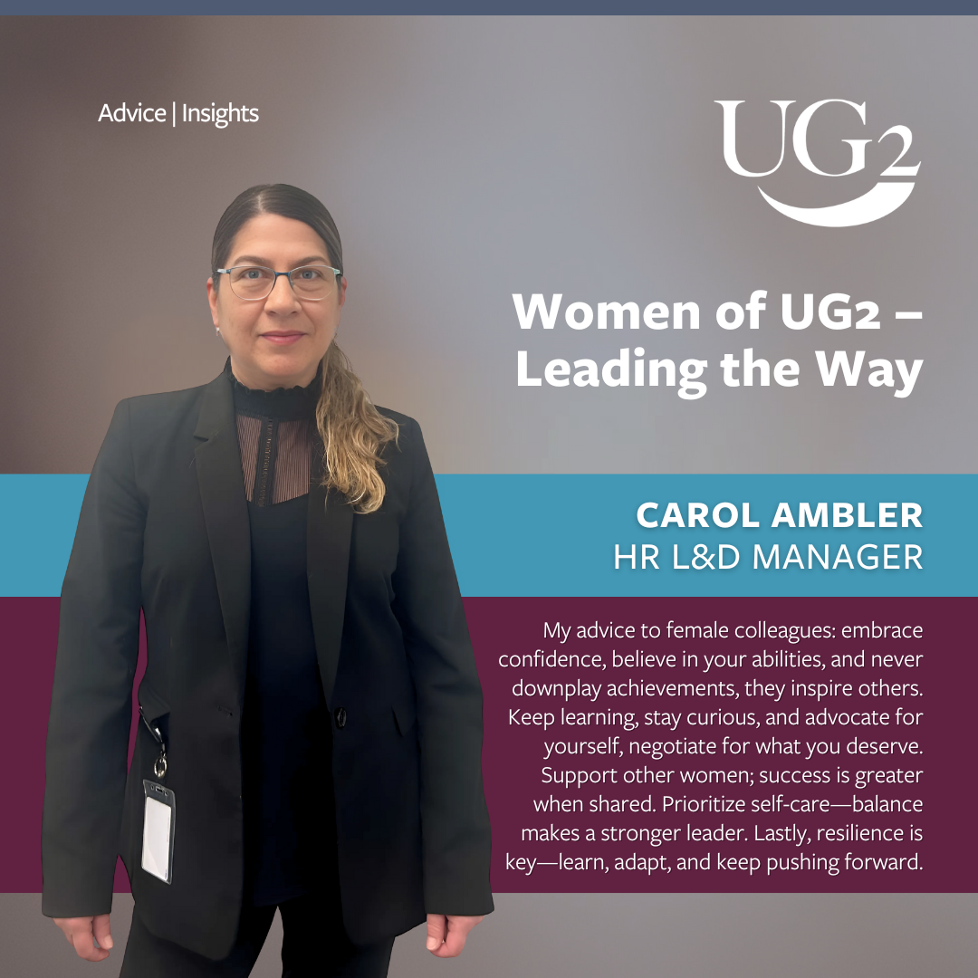 A woman in business attire stands before a sign that reads "Women of UG2 – Leading the Way," sharing essential advice for female colleagues to inspire others in leading the way within their industry.