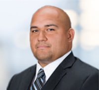A man in a dark suit and striped tie poses for a professional headshot against a blurred background, embodying the polished style often seen in Southern California business circles.