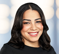 A woman with dark hair and a black top smiles at the camera in front of a blurred light background, capturing a warm moment in the Tri-State Area.