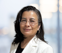 Woman with long dark hair and glasses, wearing a white blazer and black top, standing in front of a blurred indoor background, representing Midwest Integrated Facility Services.
